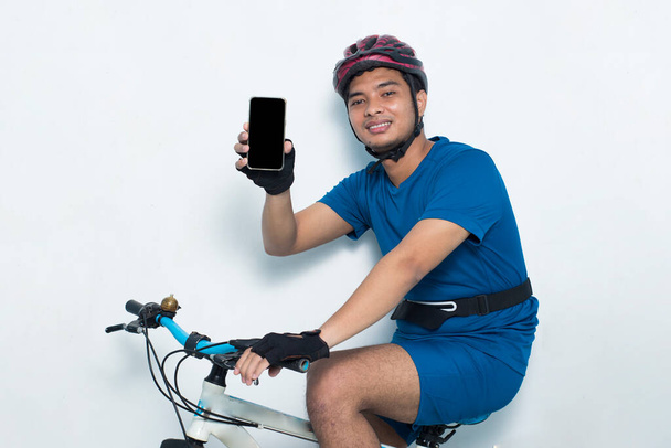 młody Azjata człowiek rowerzysta demonstrujące telefon komórkowy odizolowany na białym tle - Zdjęcie, obraz