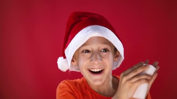 Egy vidám fiú télapó kalapban nagyon boldog, amikor szivaccsal dörzsöli a tenyerét. - Felvétel, videó