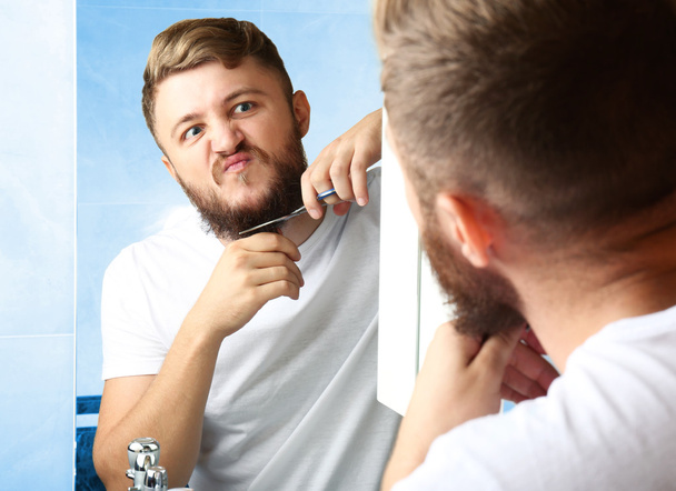 Young man shaving his beard in bathroom - Foto, imagen