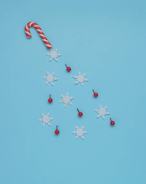 Sneeuwvlokken en snoepjes vliegen uit een kerststokje op een blauwe achtergrond. Minimalisme. Hedendaagse kunst. Het concept van het nieuwe jaar. - Foto, afbeelding