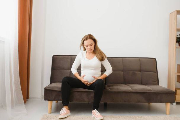 Pregnant woman getting up from sofa with hand on hip at home - Foto, immagini