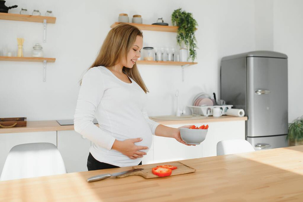 Pregnant woman in kitchen making salad - Zdjęcie, obraz