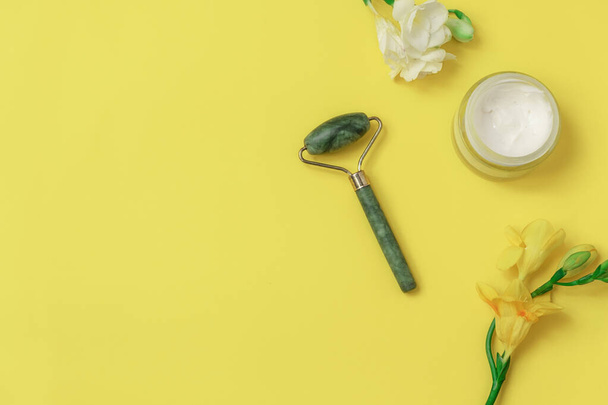 Flat lay with jade roller and flowers on yellow background. Image with copy space - Foto, afbeelding