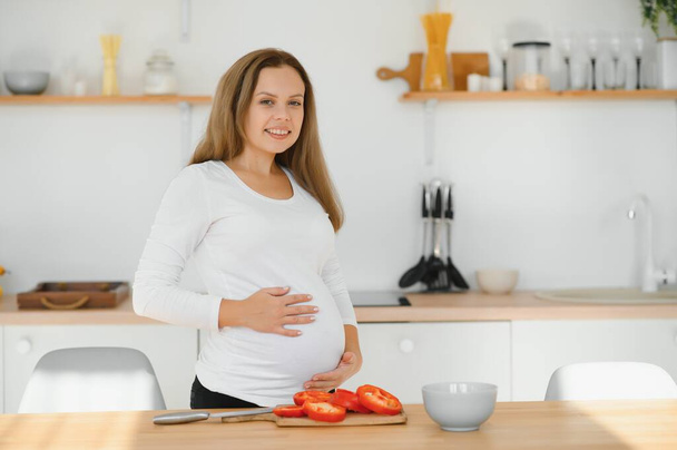 Pregnant woman in kitchen making salad - Foto, afbeelding