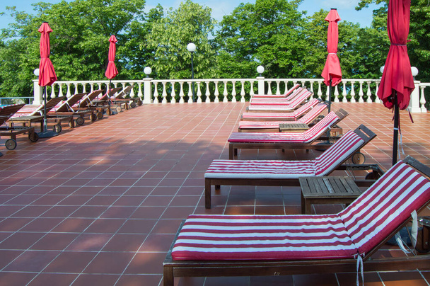 Cadeiras de madeira vazias com colchões listrados vermelhos e brancos estão em uma fileira. Luxo recreação ao ar livre, sol. - Foto, Imagem
