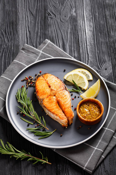 baked salmon steak with wholegrain mustard, lemon, rosemary on a plate, vertical view from above - Fotoğraf, Görsel