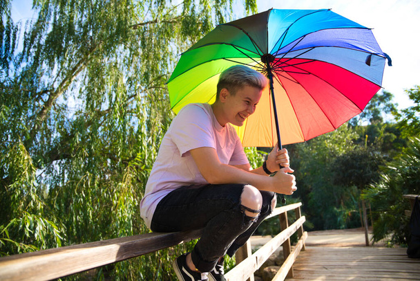 μη δυαδικό μη δυαδικό μη-δυαδικό ανδρόγυνο άτομο με γκέι ομπρέλα υπερηφάνειας. Χαμογελάει και κοιτάζει την κάμερα. Μη δυαδική και ανδρογυνική έννοια. Έννοια πολυμορφίας. - Φωτογραφία, εικόνα