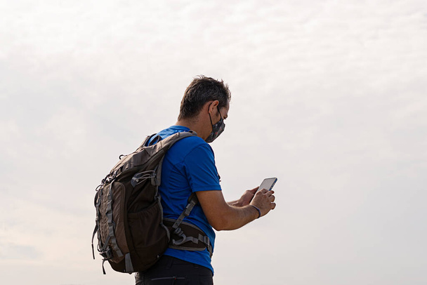 A Caucasian male with a backpack looking at a cell phone on a white background - Photo, image
