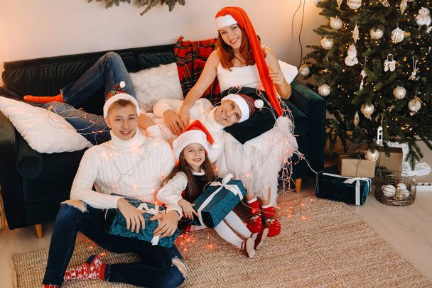 Retrato de cerca de una familia feliz sentada en un sofá cerca de un árbol de Navidad celebrando unas vacaciones. - Foto, Imagen