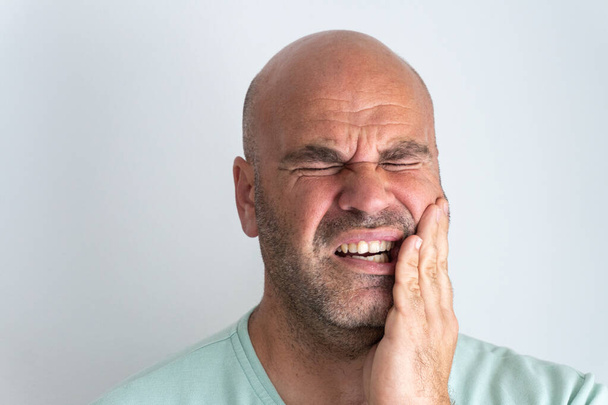 Close-up of bald, bearded Caucasian man gesturing a toothache. - Photo, Image