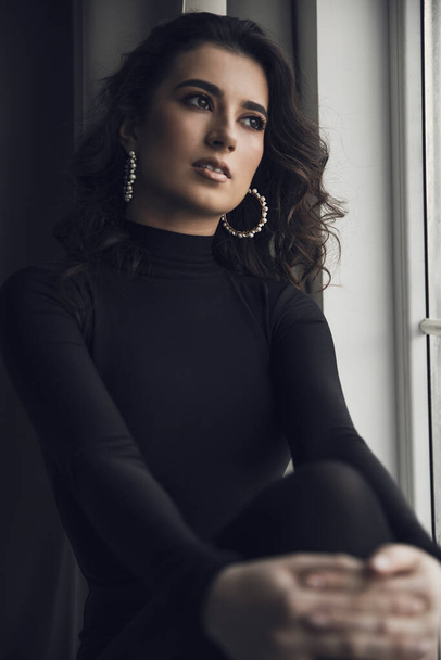 Retrato de uma jovem bonita em um bodysuit preto posando perto de grandes janelas. - Foto, Imagem