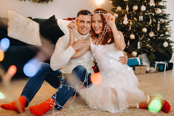 a happy married couple is sitting at home on the floor near the Christmas tree. - Photo, Image