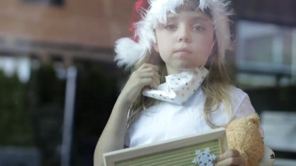 Niña de 6 años con sombrero de Santa Claus con tablero de letras donde está escrito en Geman - Feliz Navidad - Metraje, vídeo