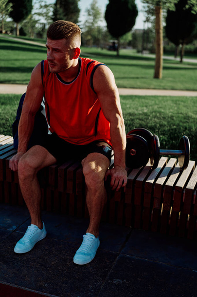 Cheerful male athlete in the park sits on a bench - Фото, изображение