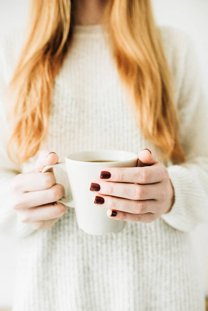Hermosa mujer con pelo rojo sostiene taza con café caliente en sus manos - Foto, imagen