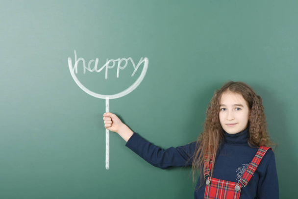 Kamaszkor előtti lány kezében festett tabletta "boldog" felirattal. Iskolai háttérrel. Nagy felbontású fotó. Teljes mélységélesség. - Fotó, kép