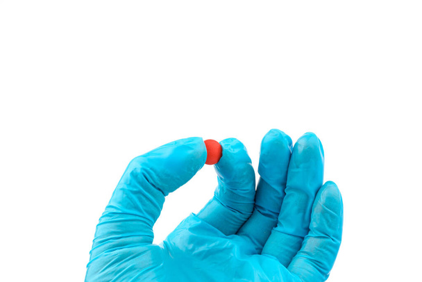 Las manos enguantadas con pastillas rojas, La mano del trabajador médico en guantes médicos sosteniendo pastillas - Foto, imagen