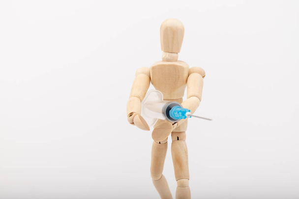 Dřevěná figurína s injekční stříkačkou na bílém pozadí. Koronavirová vakcinace. Mezera pro text. - Fotografie, Obrázek