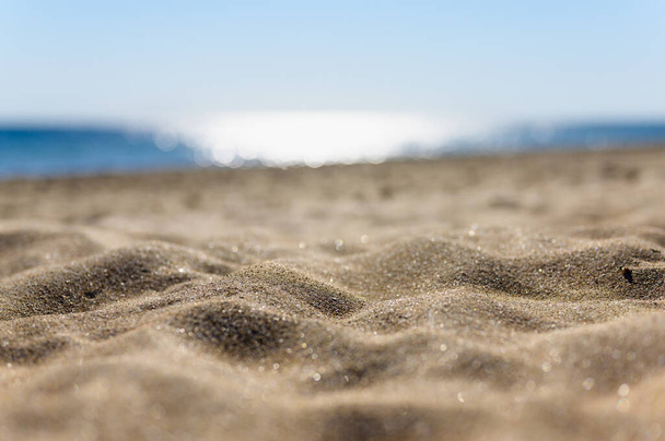 Hiekkaranta lähikuva taustaa vasten auringon häikäisyä meressä. Kapea valikoiva keskittyminen hiekkaan ja hämärtyneeseen taustaan. - Valokuva, kuva