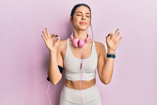 Young hispanic woman wearing gym clothes and using headphones relaxed and smiling with eyes closed doing meditation gesture with fingers. yoga concept.  - Fotografie, Obrázek