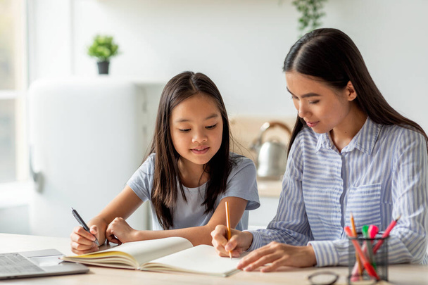 Conceito de actividades e interesses comuns. Jovem asiático mãe e filha desenho com marcadores, sentado na cozinha - Foto, Imagem