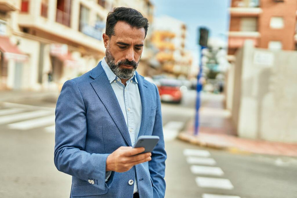 Middle age businessman with serious expression using smartphone at the city. - Photo, image