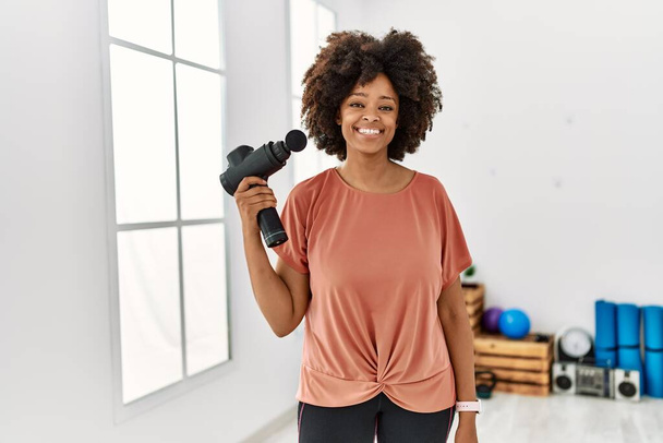 Young african american woman smiling confident holding percussion pistol at sport center - Foto, imagen