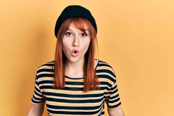 Redhead young woman wearing wool cap scared and amazed with open mouth for surprise, disbelief face  - Foto, Bild