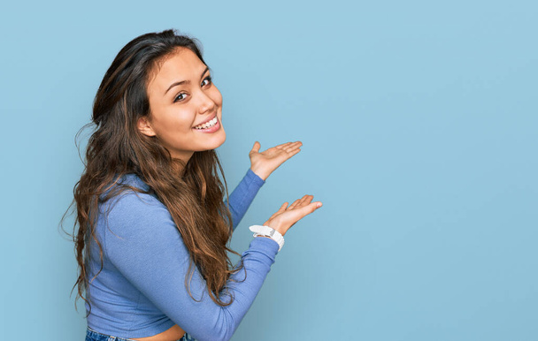 Chica hispana joven con ropa casual invitando a entrar sonriendo natural con la mano abierta  - Foto, imagen
