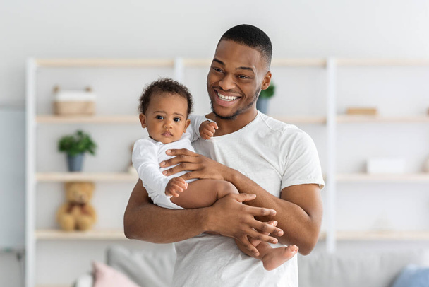 Concepto de crianza. Retrato del alegre hombre afroamericano sosteniendo a su hijo pequeño - Foto, imagen