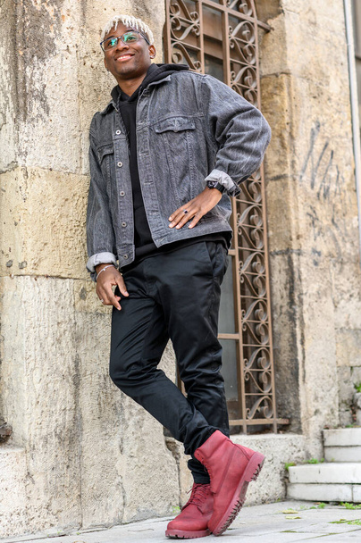 Концепция школьной молодежи. Улыбающийся афроамериканец с дредами, расслабленный у стены. Полнометражный портрет подростка - Фото, изображение