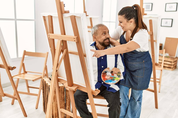 Young painting teacher woman teaching art to senior man painting on canvas at art studio - 写真・画像