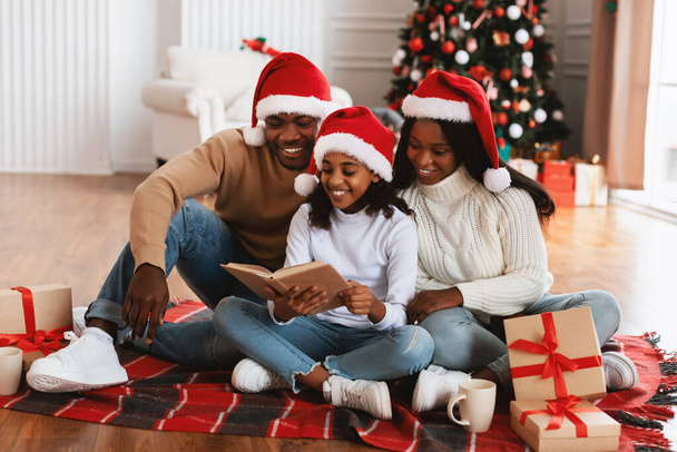 Portret van gelukkige zwarte familie in santa hants lezen boek - Foto, afbeelding