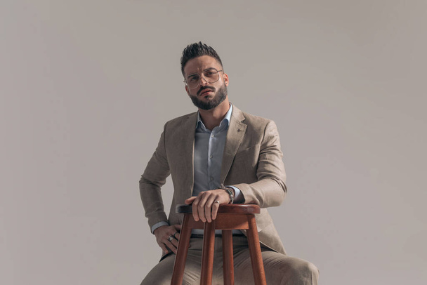 cool sexy businessman sitting like a boss and posing against gray studio background - Фото, изображение