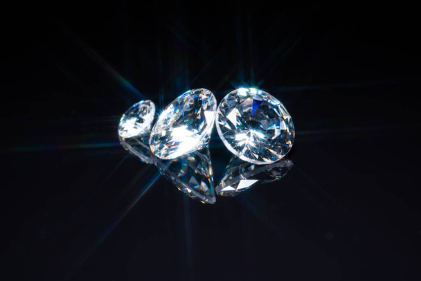 Diamonds selective focus on black reflective background. Polished gem stones of different size cuts. Light reflect as star shape ray burst, starburst or sunbeam. High quality brilliant jewel display. - Foto, imagen