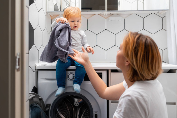 Мати і її маленька донька завантажують пральню в пральну машину разом
. - Фото, зображення