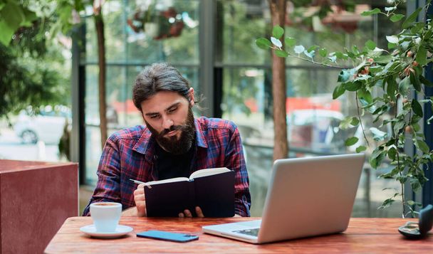 Attractive hipster guy enjoying free time and planning to do list in notebook - Photo, Image