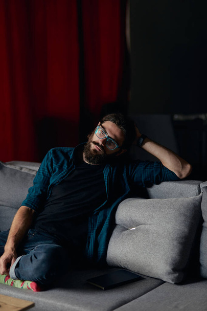 Σκεπτόμενος hipster τύπος στοχαστικός κοιτάζοντας μακριά και σκέφτεται σε εσωτερικούς χώρους, ενώ κάθεται σε έναν καναπέ. - Φωτογραφία, εικόνα