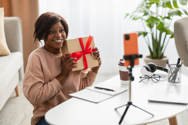 African Woman Showing Wrapped Gift Box To Smartphone At Home - Φωτογραφία, εικόνα