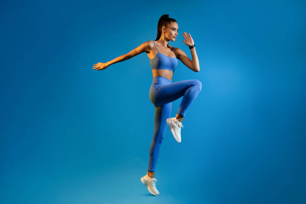 Vrouwelijke atleet springen oefening tijdens de training over Blue Studio achtergrond - Foto, afbeelding