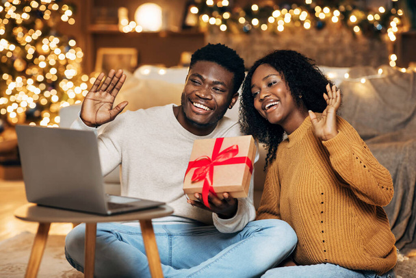 Vidám fekete pár Xmas ajándék doboz videohívás laptop, üdvözlő barátok karácsonyt online otthonról - Fotó, kép