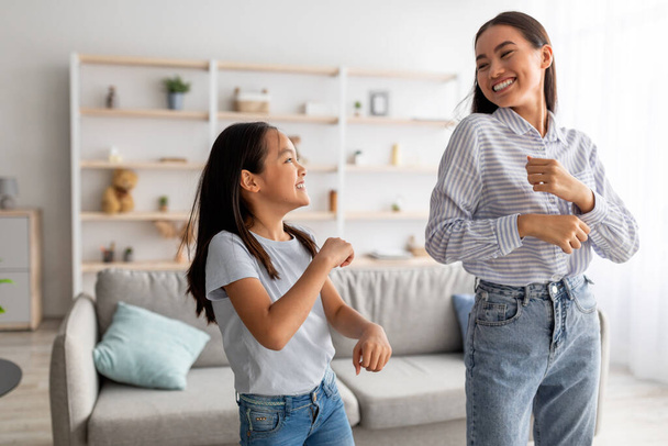 Excited asian mom and cute daughter dancing to music and having fun at home, smiling to each other - Fotografie, Obrázek