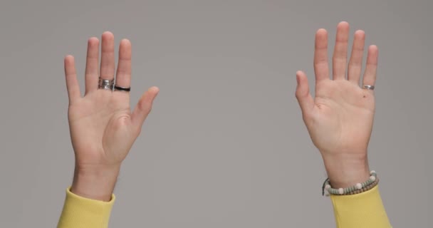 man handen in gele hoodie met ringen en armbanden knippen vingers in de voorkant van grijze achtergrond in de studio - Video