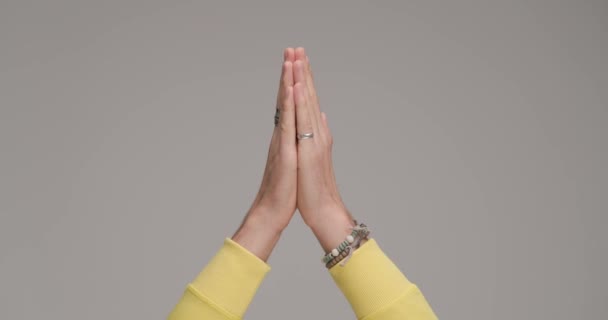 casual man's with rings and bracelets hands in the air touching and praying in front of grey background in studio - Footage, Video