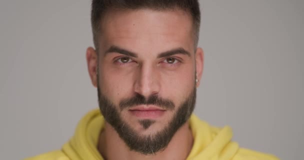 Nahaufnahme-Video eines gutaussehenden bärtigen Mannes in gelbem Sweatshirt, der auf grauem Hintergrund im Studio lächelt und glücklich ist - Filmmaterial, Video