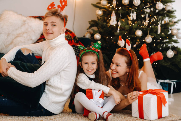 a happy family is lying on the floor of the house with New Year's gifts, next to the Christmas tree, - Foto, Imagen