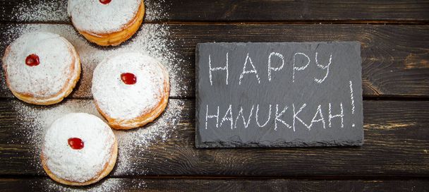 Feliz Hanukkah. Postre tradicional Sufganiyot sobre fondo de madera oscura. Donuts, velas y regalos. Celebrando la fiesta religiosa judía. Formato de banner. - Foto, imagen