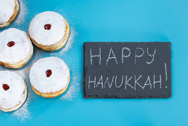 Happy Hanukkah. Jewish dessert sufganiyot donuts on blue background. Symbol of religious Judaism holiday. Inscription on the chalk board. - Foto, immagini