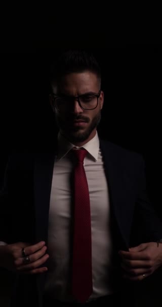 δραματική γενειοφόρος επιχειρηματίας με γυαλιά στερέωση και κλείσιμο κοστούμι, κρατώντας τα χέρια και ξεθώριασμα μακριά στο σκοτάδι - Πλάνα, βίντεο