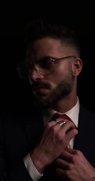 красивий незадоволений бізнесмен з металевими каркасними окулярами, дивлячись на бік, фіксуючи краватку і перетинаючи руки, киваючи перед чорним тлом
 - Кадри, відео